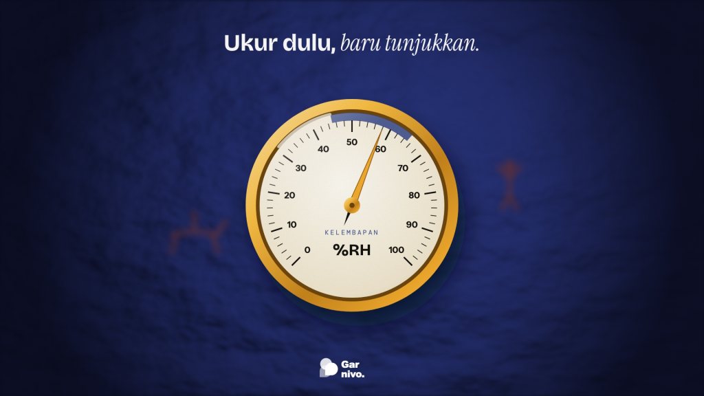Higrometer berbingkai kuningan dengan jarum amber di zona aman kelembapan, di depan dinding gua nila yang kabur berhias gambar oker.