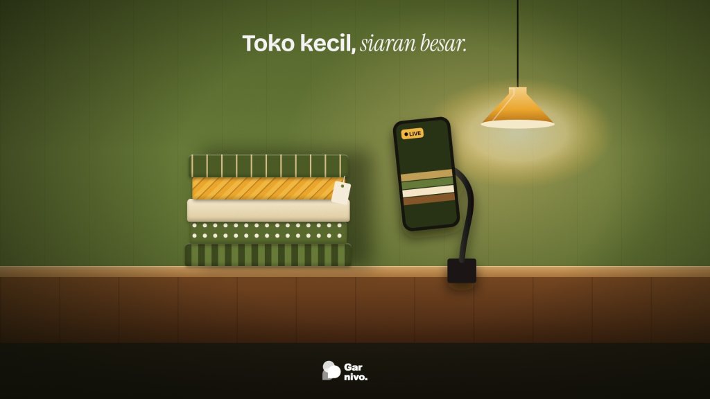 Tumpukan kain bermotif di meja kayu toko kecil, ponsel berpenjepit leher angsa menyiarkan LIVE, di bawah lampu gantung amber.