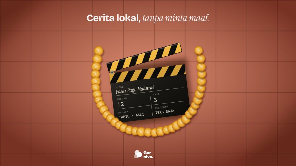 Papan klip film hitam bergaris amber di lantai ubin terakota, dikelilingi untaian bunga amber; isian kapur menyebut bahasa Tamil asli.